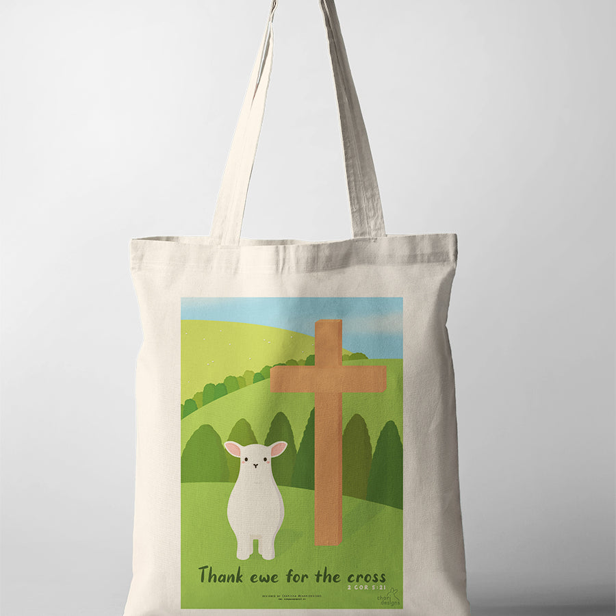 Christian canvas tote bag featuring a cute lamb beside a wooden cross with the phrase “Thank ewe for the cross” inspired by 2 Corinthians 5:21, collaboration with Chari Designs.