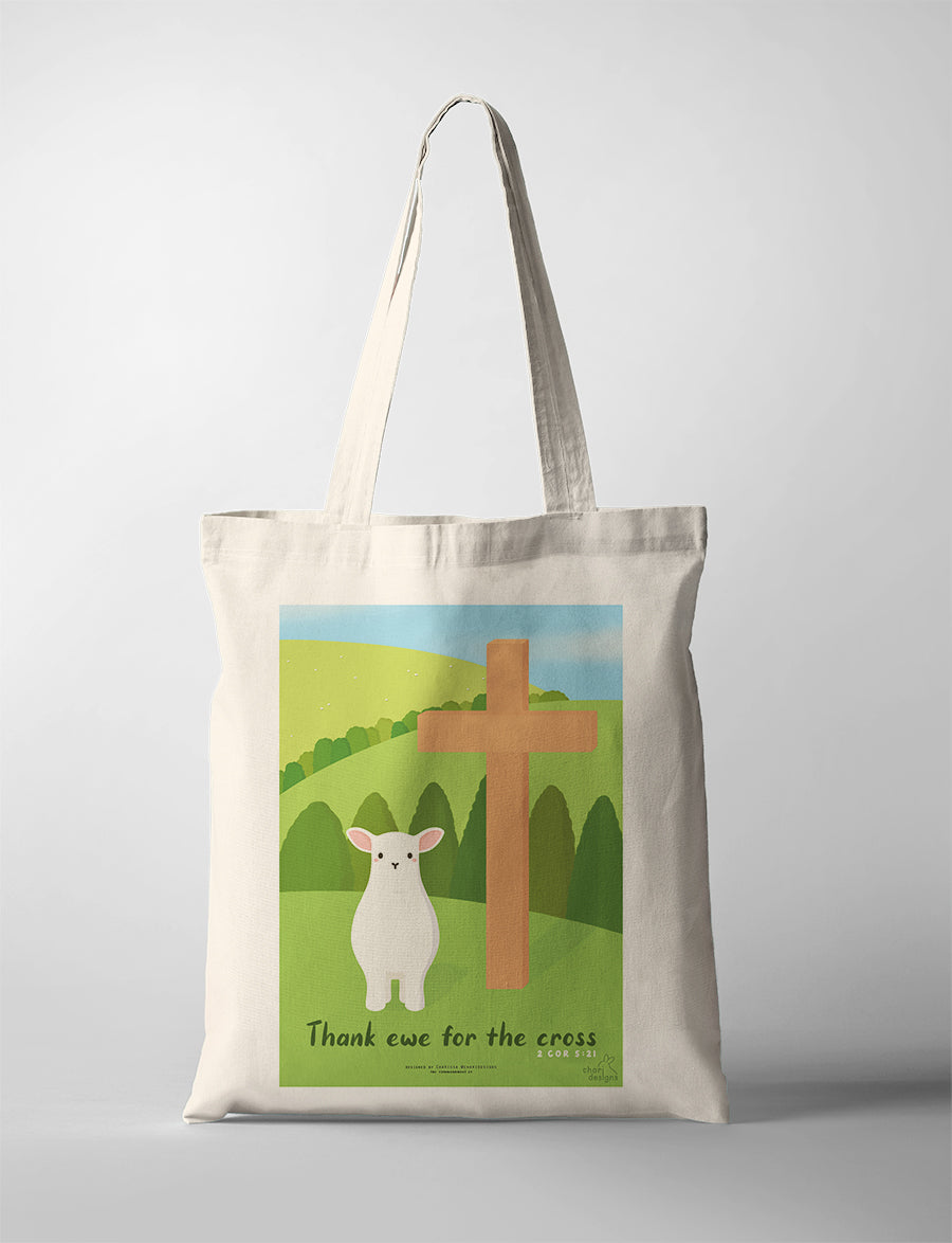 Christian canvas tote bag featuring a cute lamb beside a wooden cross with the phrase “Thank ewe for the cross” inspired by 2 Corinthians 5:21, collaboration with Chari Designs.