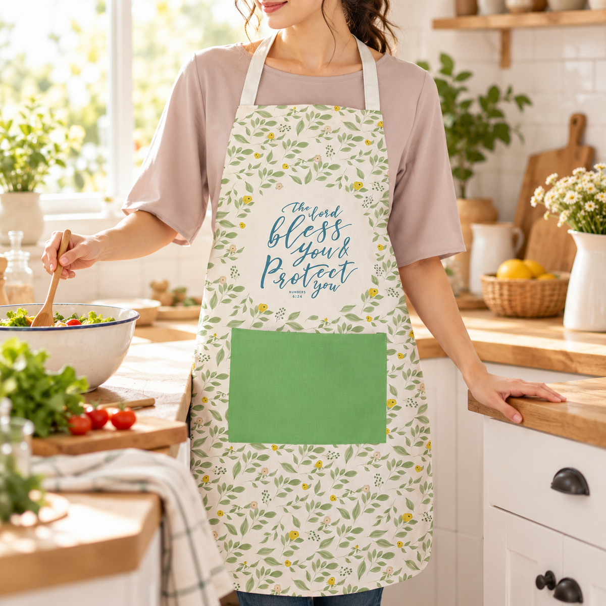 The Lord Bless You and Protect You Christian apron with floral pattern and green pocket worn while preparing food in a bright warm kitchen