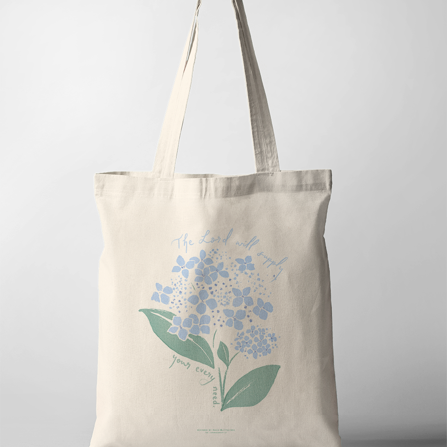 Neutral canvas tote bag featuring a delicate blue hydrangea illustration and the uplifting message "The Lord will supply your every need," inspiring simple happiness and faith-filled encouragement.