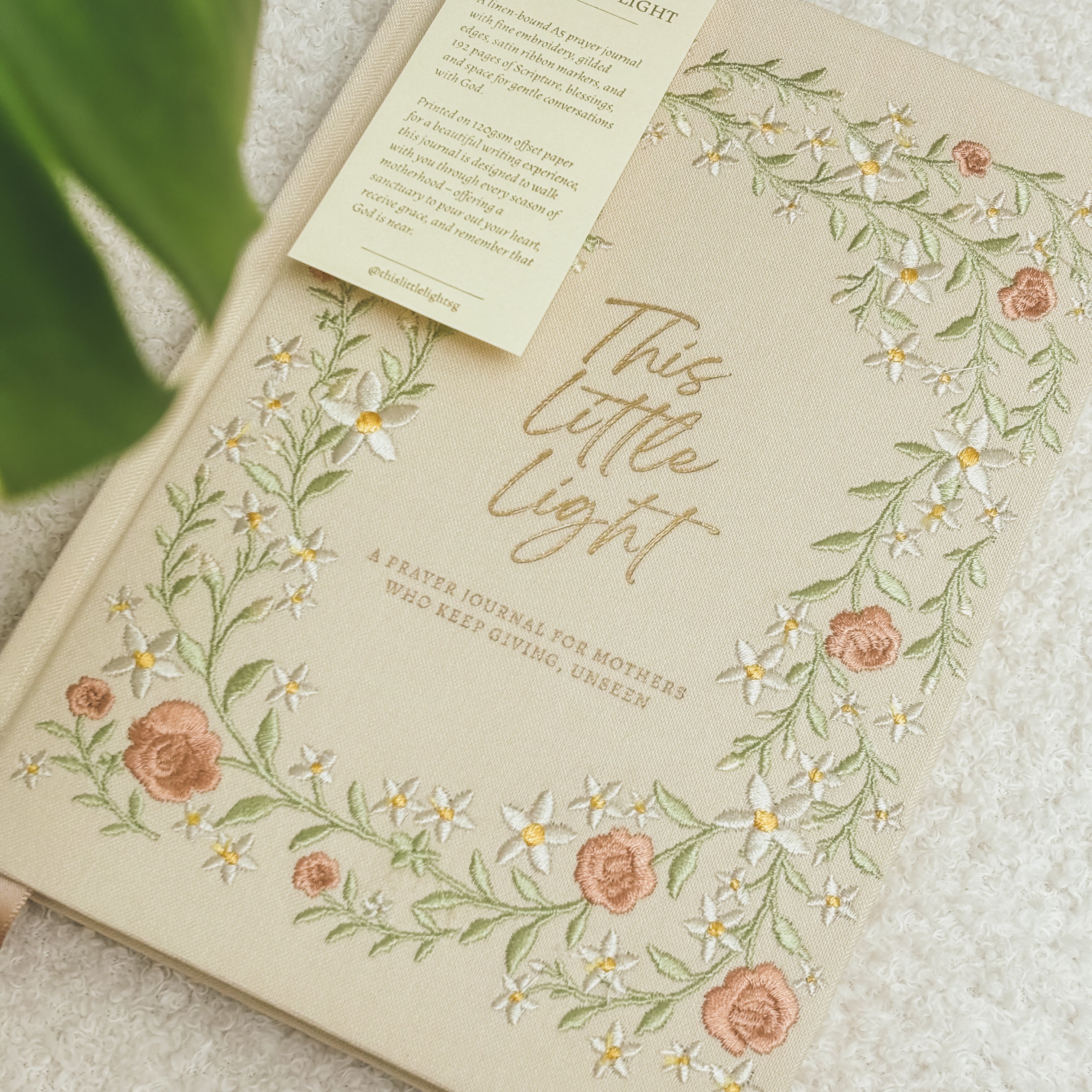 This Little Light floral prayer journal for mothers styled on a white chair with ribbon bookmarks