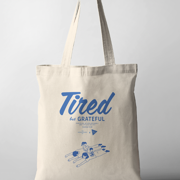 Tote Bag with the phrase "Tired But Grateful" featuring an illustration of parents lying down with two kids on them — a heartfelt design celebrating parenthood and faith.