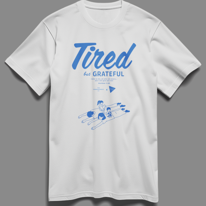 Christian t-shirt with the phrase "Tired But Grateful" featuring an illustration of parents lying down with two kids on them — a heartfelt design celebrating parenthood and faith.