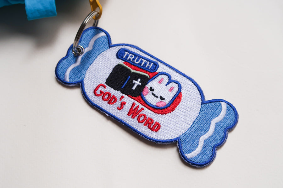 Close-up of embroidered candy-shaped Bible verse keychain reading “’Tis So Sweet to Trust in Jesus