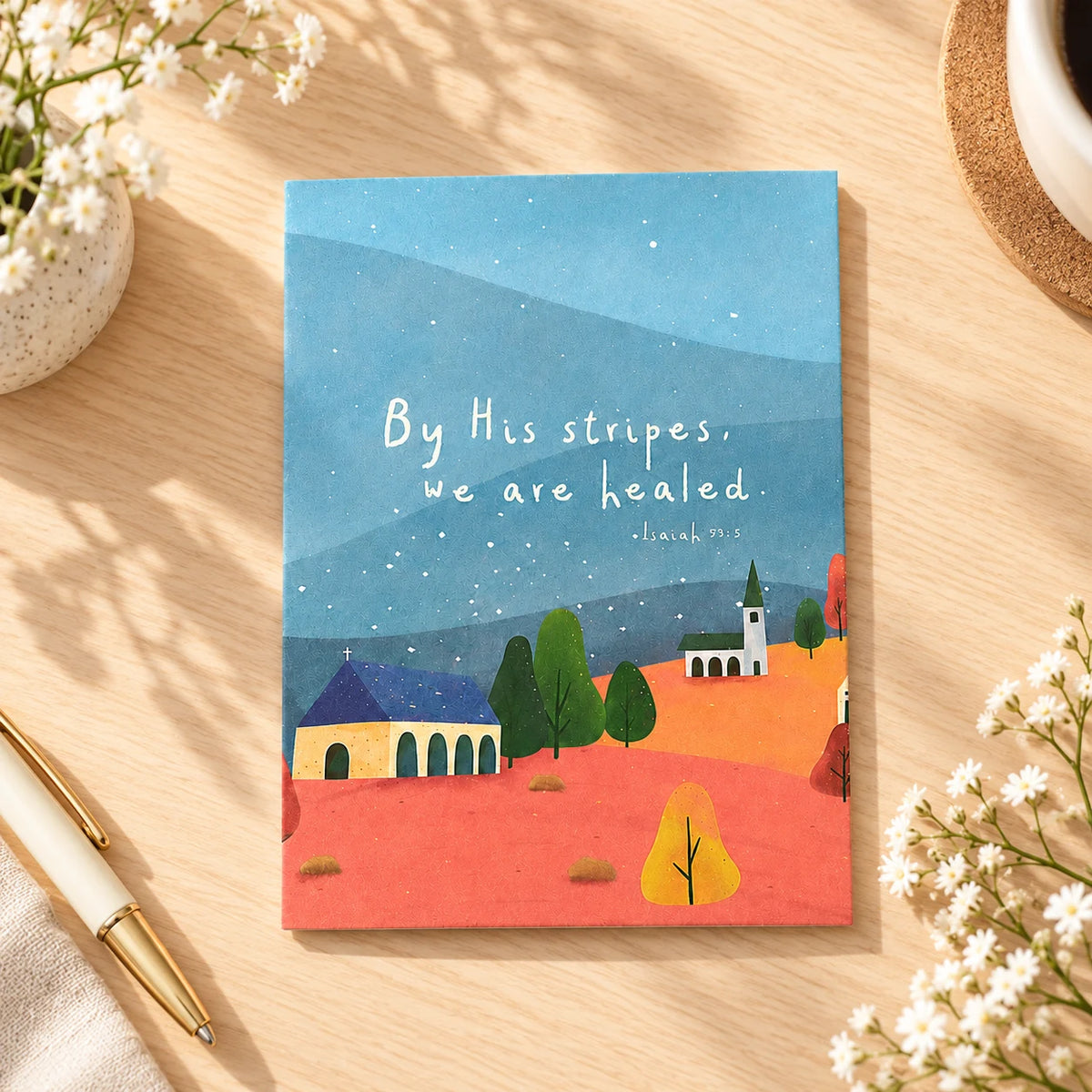 By His Stripes We Are Healed Isaiah 53:5 Christian card lying flat on a warm wooden desk with flowers and pen