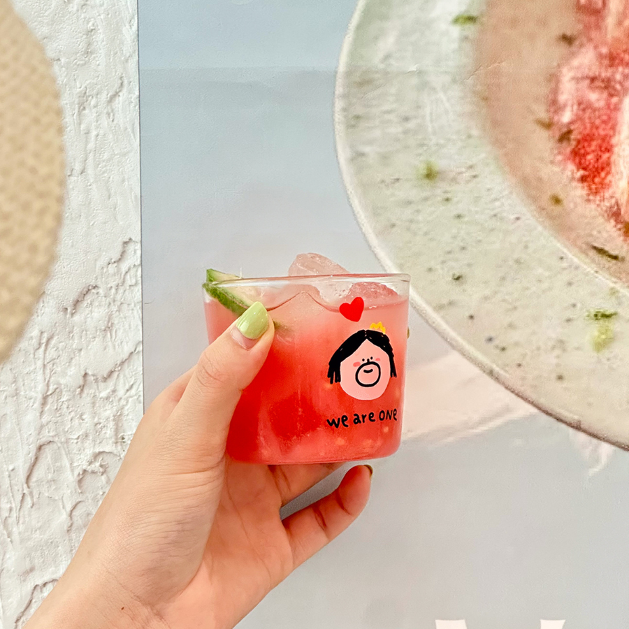 Glass mini cup with "We are one" design, filled with a refreshing drink, symbolizing unity.