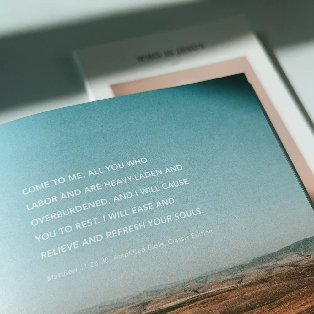 An open page from the Who Is Jesus book featuring an encouraging Bible verse from Matthew 11:28-30, inviting rest and refreshment, with the book cover in the background, reflecting simple happiness and faith.