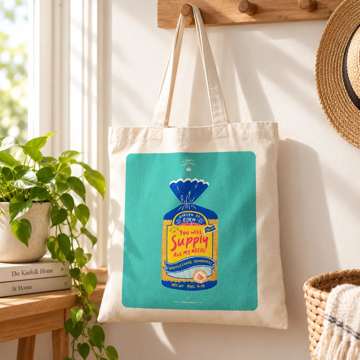 Wholesome Bread Pack Christian canvas tote bag with colourful bread-inspired Philippians 4:19 artwork hanging in a sunny entryway