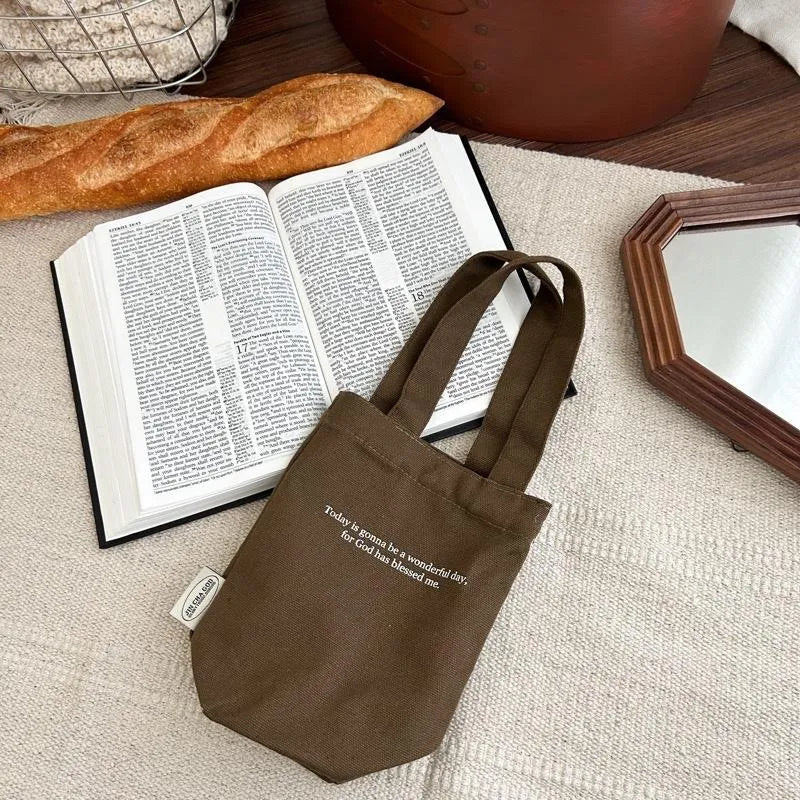 Brown canvas drink carrier bag with “Today is gonna be a wonderful day, for God has blessed me” text beside an open Bible