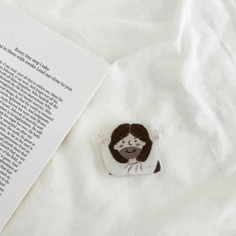 Close-up of the YA! Jesus hand-drawn phone grip featuring a cute Jesus illustration beside an open devotional page