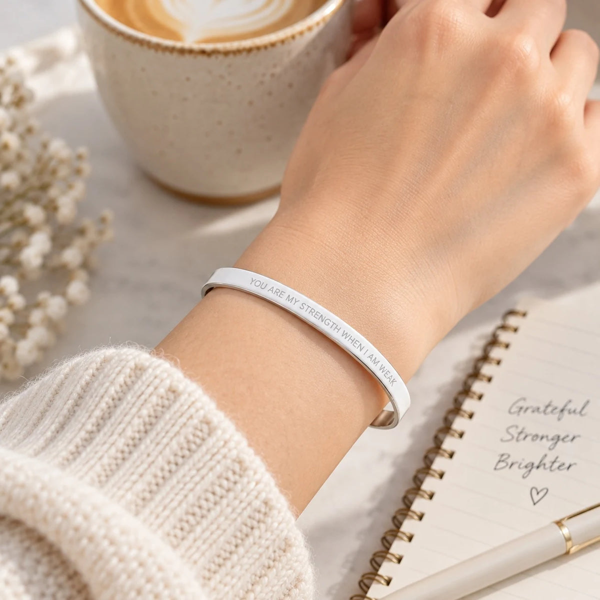 Silver You Are My Strength When I Am Weak engraved verse band worn on a wrist beside a journal and coffee.