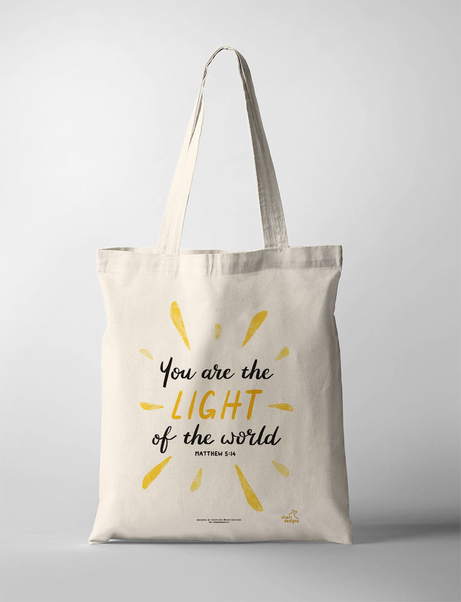 Christian tote bag featuring the Bible verse “You are the light of the world” Matthew 5:14 with yellow sunburst design, collaboration with Chari Designs.