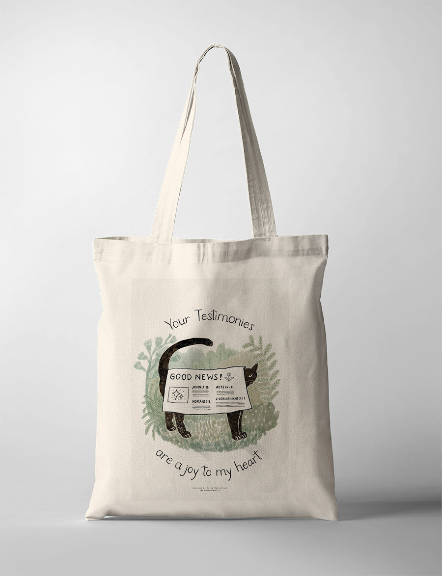 Christian tote bag featuring “Your testimonies are a joy to my heart” with a black cat holding a Good News newspaper