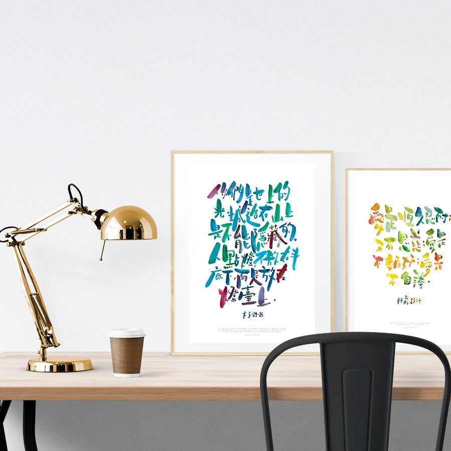 A3 beautiful calligraphy poster placed standing next to a smaller A4 sized calligraphy poster on a wooden table. Modern Christian home interior design ideas.
