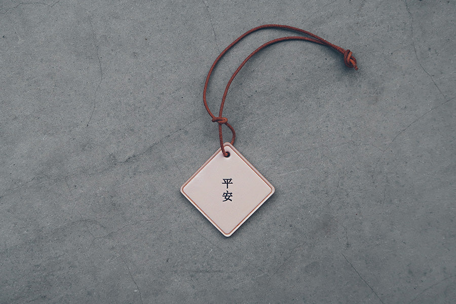 Double-sided leather car charm with English Peace and Chinese Ping An engraving.