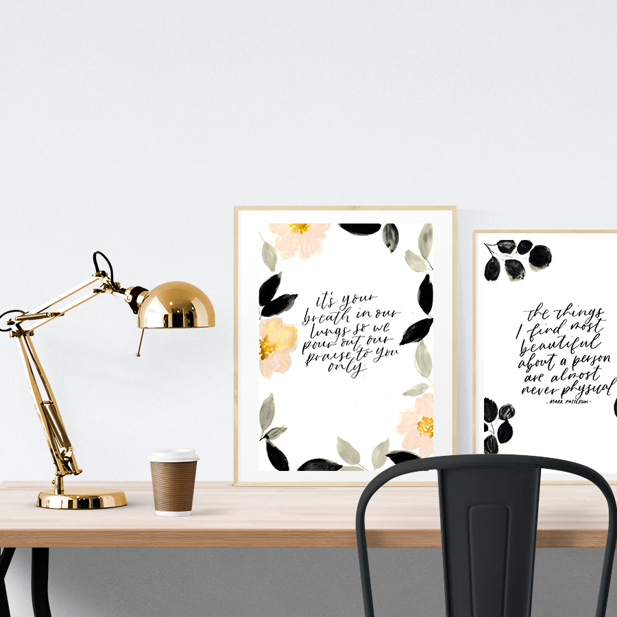 A3 beautiful calligraphy poster placed standing next to a smaller A4 sized calligraphy poster on a wooden table. Minimalistic Christian home interior design ideas.