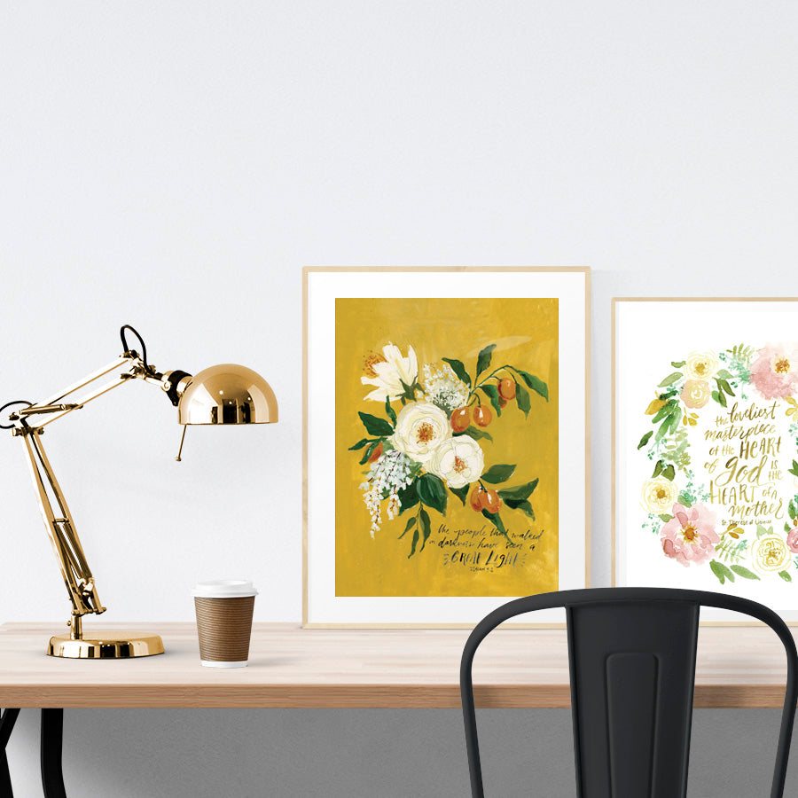 A3 beautiful painting poster placed standing next to a smaller A4 sized floral calligraphy poster on a wooden table. Inspiring home decor ideas.