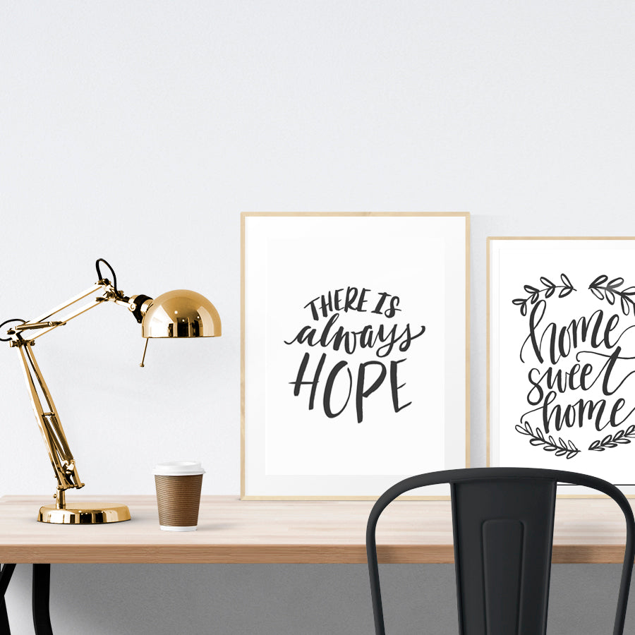 A3 beautiful calligraphy poster placed standing next to a smaller A4 sized calligraphy poster on a wooden table. Minimalistic home interior design ideas.