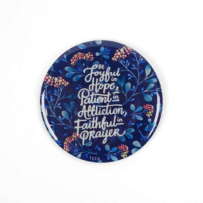 5.5 cm diameter circular Acrylic fridge magnet with bible verse “Be joyful in Hope, patient in affliction, faithful in prayer” on foliage background.