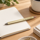 Hex Classic personalised brass ballpoint pen engraved Be Strong and Take Heart on an open notebook in a warm sunlit desk setting