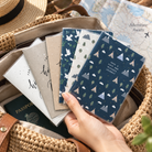 Have a Safe and Blessed Journey Christian passport covers held above an open travel bag with passport and map