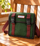 10th Anniversary Good News green canvas postman sling bag styled on a wooden chair.