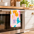 Loved Daily by Jesus colourful Christian tea towel hanging in one layer from an oven handle in a bright modern kitchen
