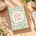 Trust in the Lord with all your heart A6 Christian notebook styled on a warm wooden desk with coffee, greenery and a pen