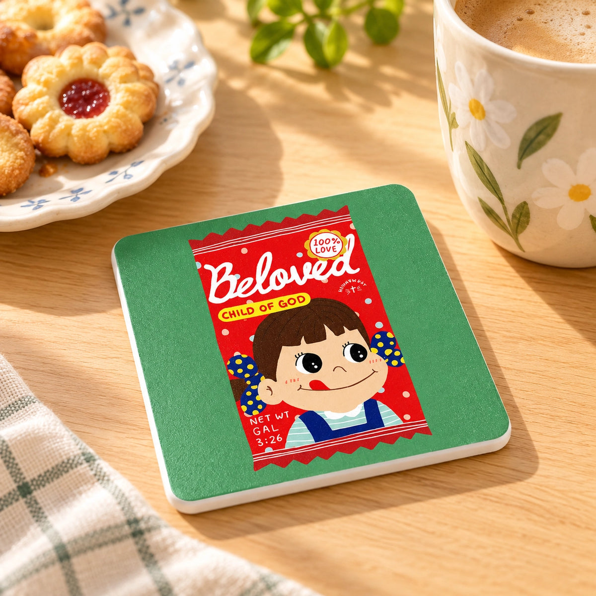 Beloved Child of God Candy Love Supermarket coaster styled beside a floral mug and biscuits on a warm wooden table