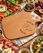 Life's Greatest Blessing wooden serving board styled with vegetables, fruit, charcuterie and tableware in warm natural light