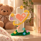 Hope Like Light micro block cross building set displayed on a shelf with books and a teddy bear.