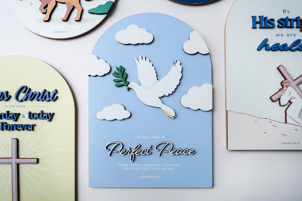 3D wooden Christian wall decor featuring a white dove holding an olive branch, surrounded by clouds, with the phrase 'Perfect Peace' and the Bible verse Isaiah 26:3.