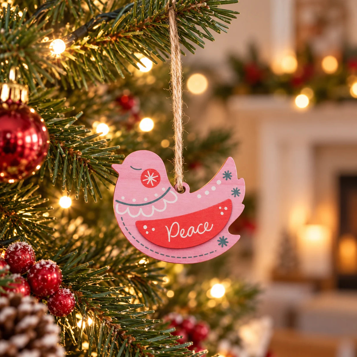 Pink Peace wooden dove Christmas bauble hanging on a warmly lit Christmas tree
