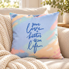 Better Than Life pastel blue and pink Christian cushion cover styled on a cream sofa with a knitted throw.