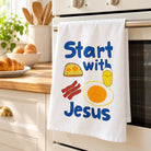 Start With Jesus tea towel hanging over an oven handle in a sunlit kitchen