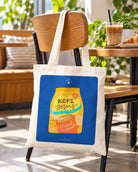 Kopi Jesus Coffee tote bag hanging from a café chair beside an iced coffee