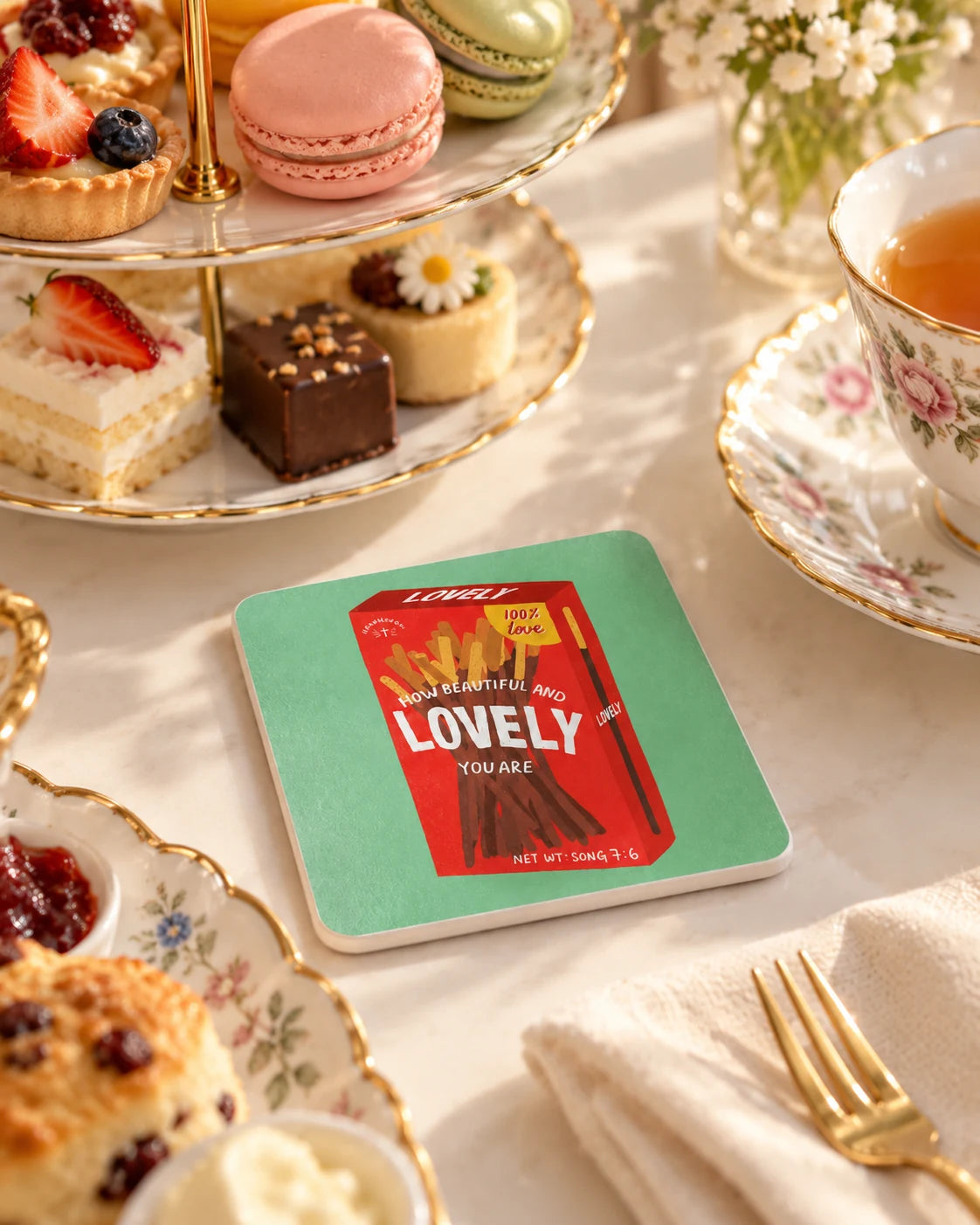 Lovely Chocolate Sticks coaster with red chocolate sticks illustration on a pastel green background, styled beside afternoon tea, macarons and pastries