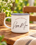 White Super Mum enamel mug with navy rim and 'Specially Brewed for Super Mum' lettering on a sunlit wooden table