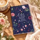 Love Always A5 Christian notebook with navy floral cover on a wooden desk beside a cup of coffee and pen