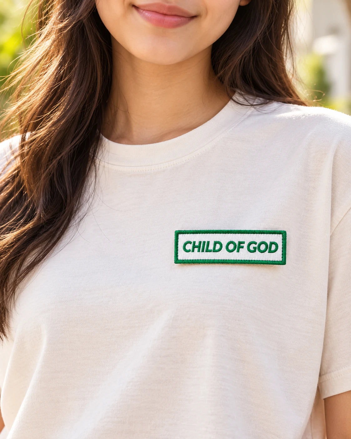 Green Child of God embroidered Velcro tag attached to the front of a white T-shirt