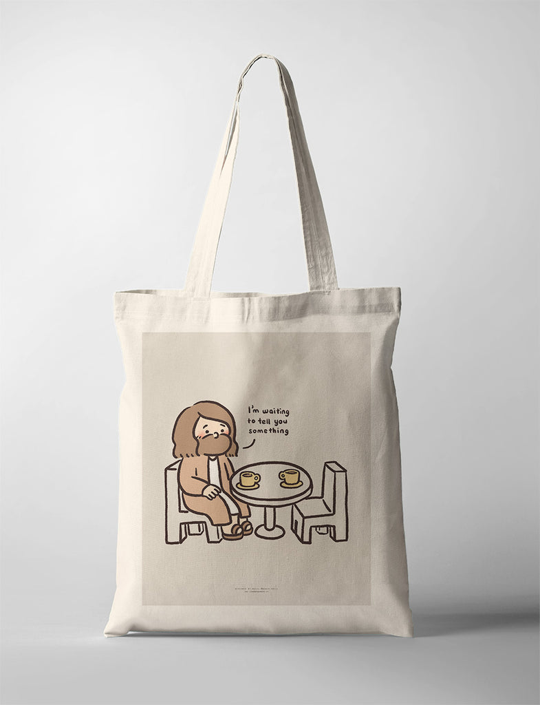 Canvas tote bag featuring a playful illustration of Jesus sitting at a table with coffee cups, saying 'I'm waiting to tell you something,' symbolizing patience and connection.