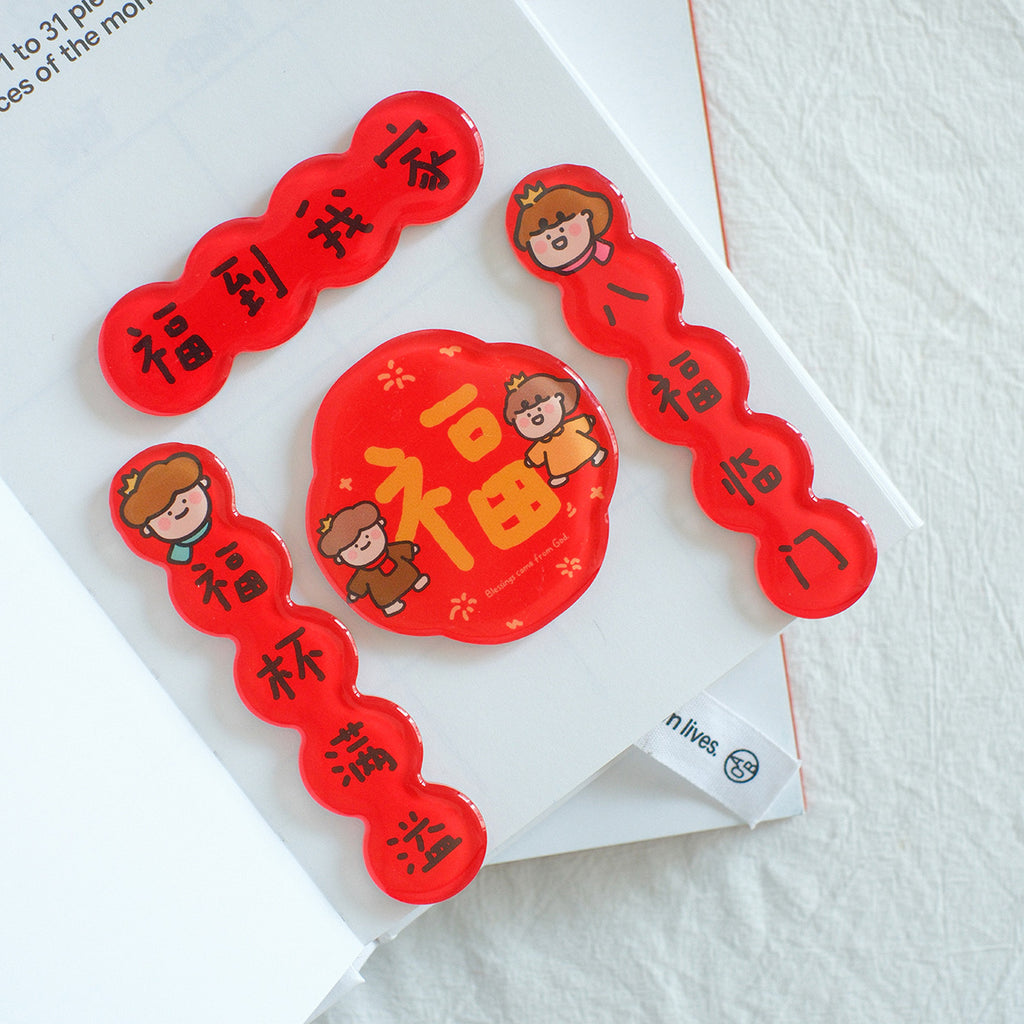 Red Chinese New Year couplet magnets with blessings and prosperity messages, featuring cute character designs, placed on a white planner