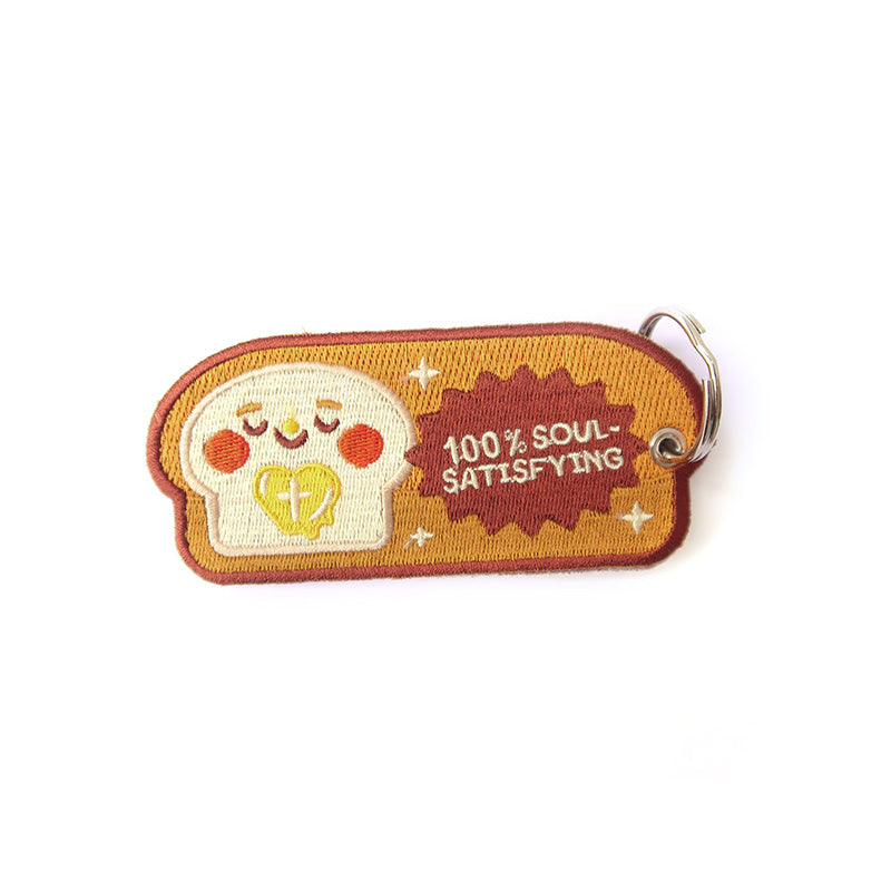 Cute bread-themed keychain with an embroidered smiley face and the phrase '100% Soul-Satisfying'.