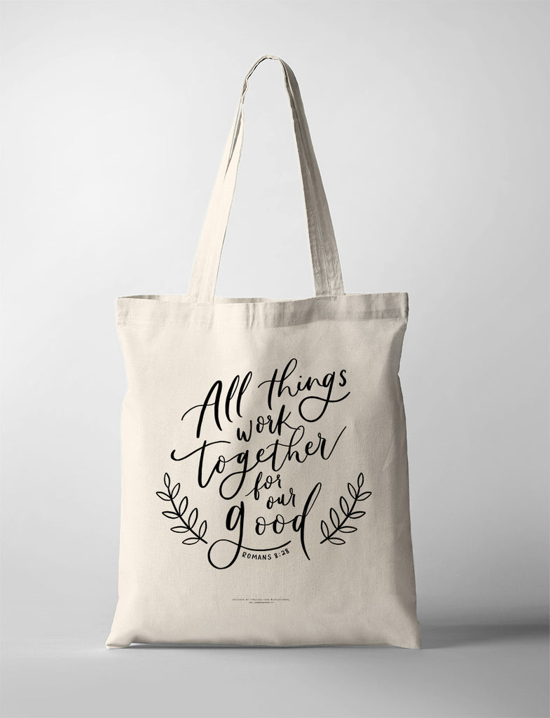 Minimalist tote bag design with the verse 'All things work together for our good - Romans 8:28' in black calligraphy.