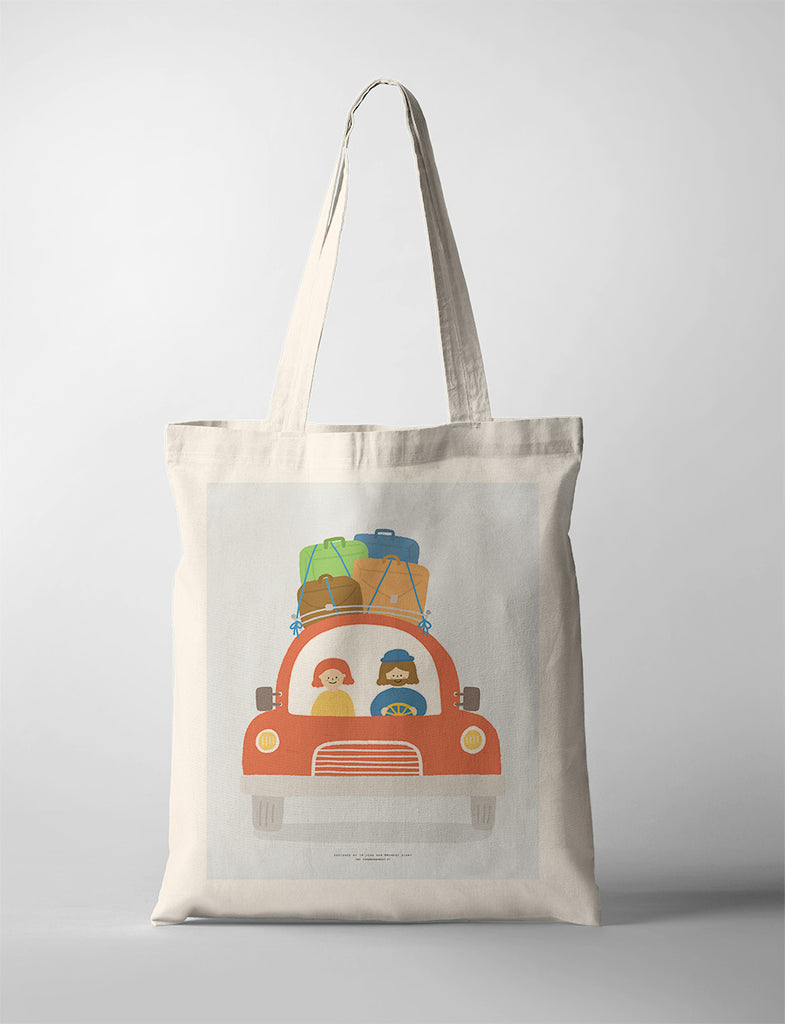 Eco-friendly canvas tote bag featuring an illustration of a cheerful road trip scene with two characters in a red car, luggage secured on the roof, symbolizing adventure and travel.