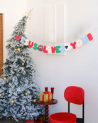 Jesus Loves You Party Banner hanging beside a Christmas tree, featuring colorful lettering and 18 unique Christian-themed patterns. Perfect for Christian celebrations, church events, and home décor.