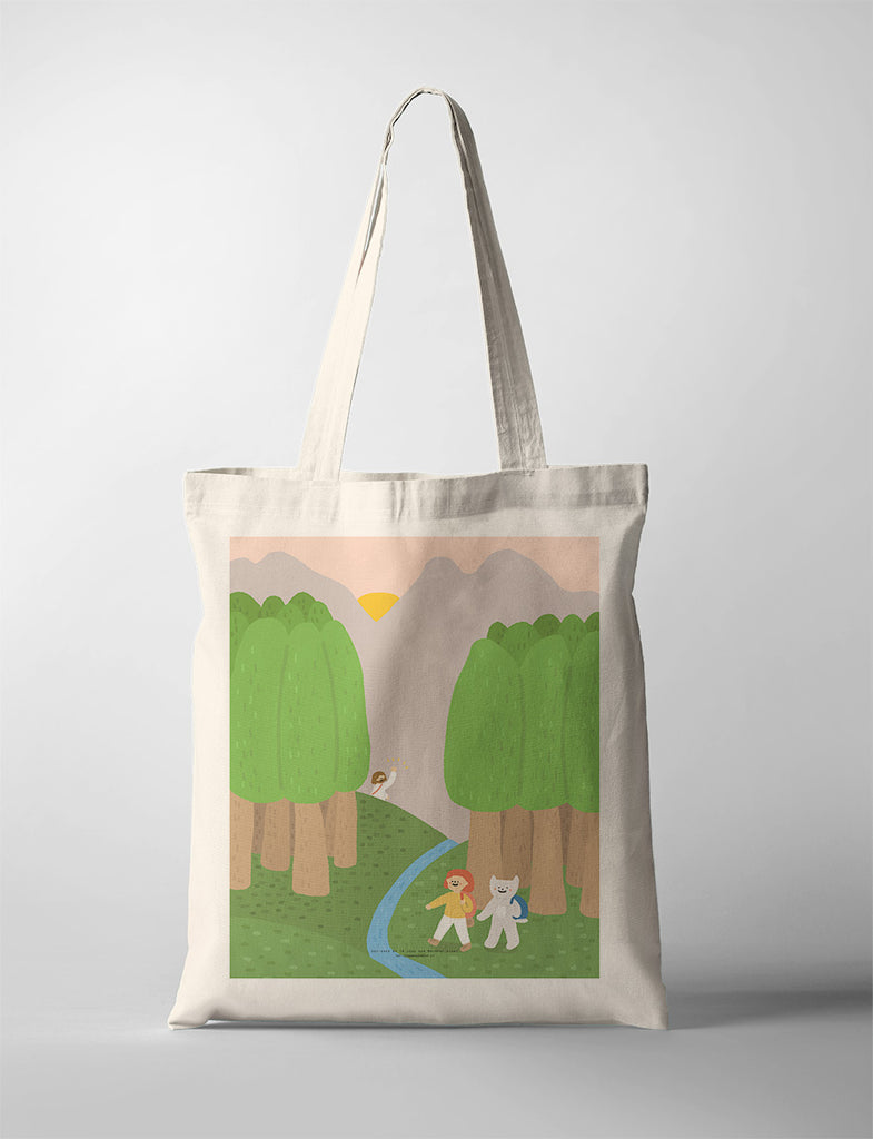 Eco-friendly canvas tote bag featuring an illustration of two cheerful characters walking through a lush green forest with a flowing stream, under a serene sunset sky, symbolizing adventure and nature.