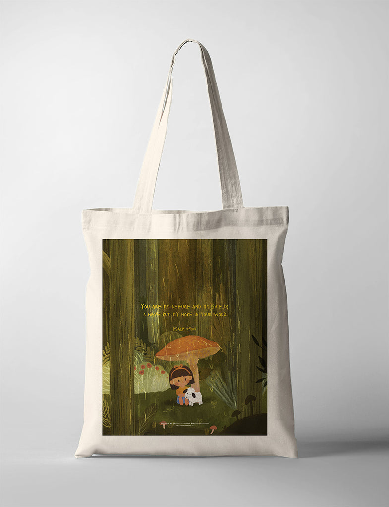 A beige tote bag featuring a Christian-themed illustration of a child sitting under a large mushroom with a small white dog. The design includes the Bible verse from Psalm 119:114: 'You are my refuge and my shield; I have put my hope in your word,' conveying a message of comfort and faith.