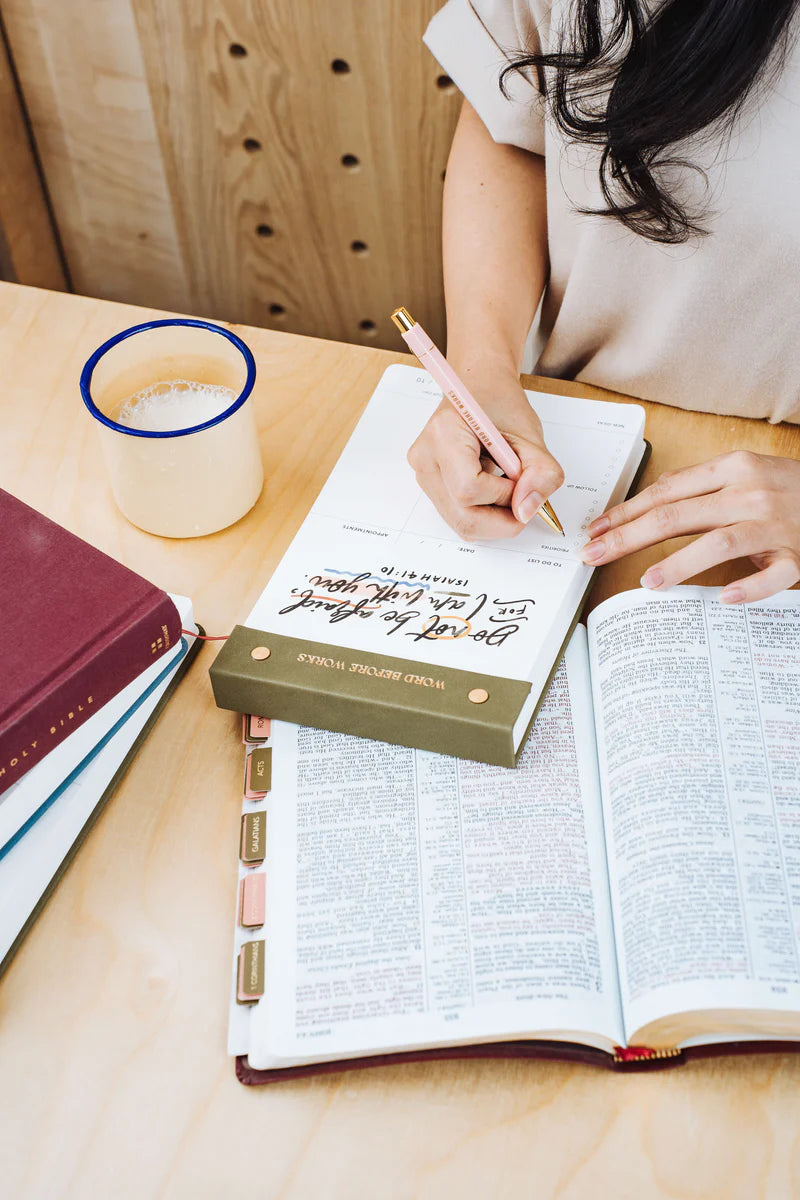 Woman writing on The Project J Christian notepad with "Do not be afraid, for I am with you" from Isaiah 41:10, alongside an open Bible and a cup of coffee, inspiring peaceful and faith-filled daily planning.