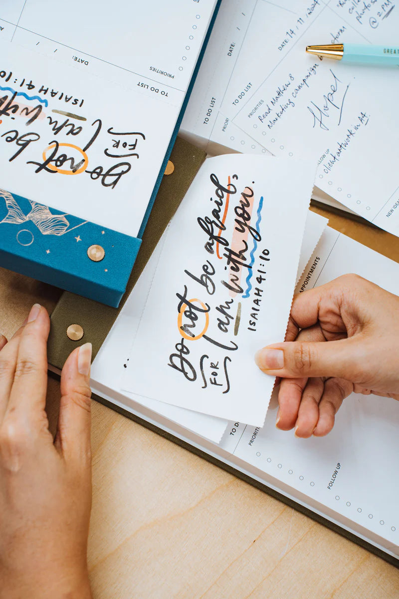  Hands tearing a page from The Project J Christian notepad featuring the inspiring verse "Do not be afraid, for I am with you" from Isaiah 41:10, perfect for uplifting daily planning and encouragement.